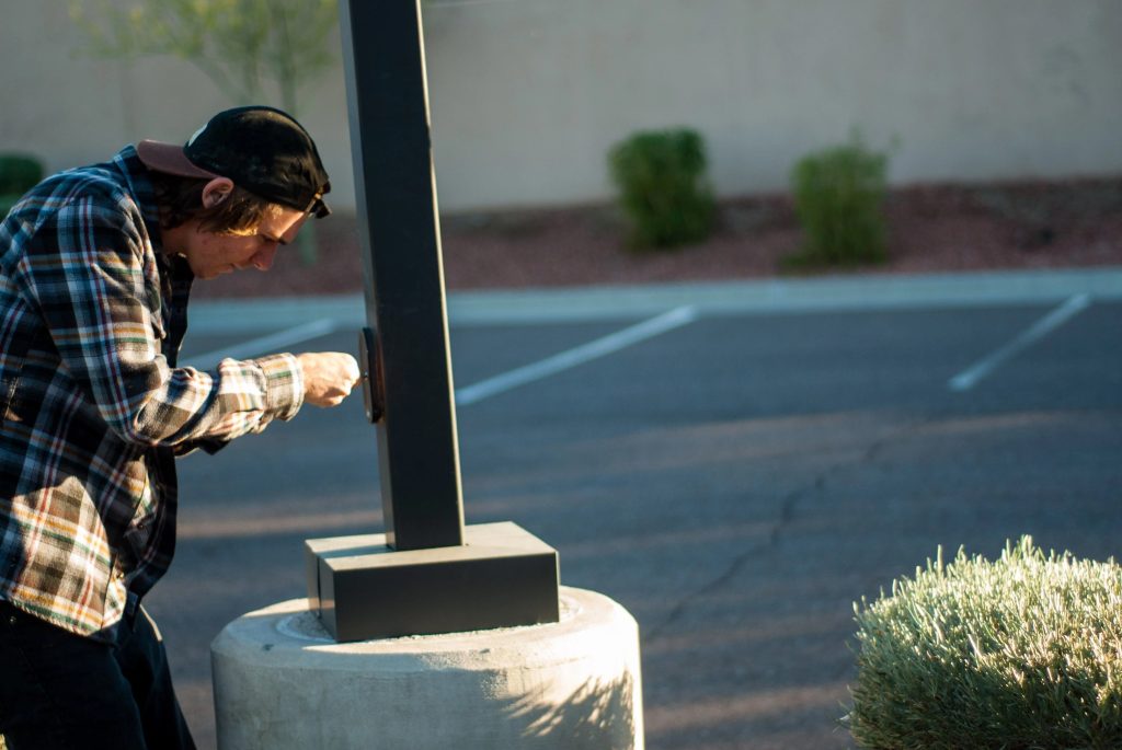 Tradesmen performing installing End Metal Theft Hand Hole Cover on light pole in empty parking lot.